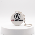 A white circular A-Spec keychain featuring the black Acura logo and red A-SPEC text, attached to a silver metal chain, displayed on a white cylindrical pedestal against a white background.