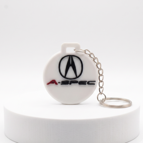 A white circular A-Spec keychain featuring the black Acura logo and red A-SPEC text, attached to a silver metal chain, displayed on a white cylindrical pedestal against a white background.