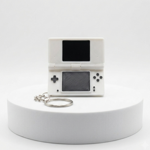 A miniature white handheld game console keychain replica with a black screen and silver keyring, displayed on a white cylindrical pedestal against a white background.