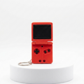 A red handheld game console keychain with a small screen and directional buttons, displayed on a white cylindrical pedestal against a white background.