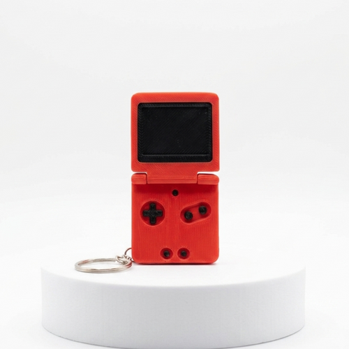 A red handheld game console keychain with a small screen and directional buttons, displayed on a white cylindrical pedestal against a white background.