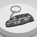 A car-shaped keychain with a silver split ring and chain, featuring a detailed grayscale illustration of a sports car, displayed on a round white pedestal against a light gray background.