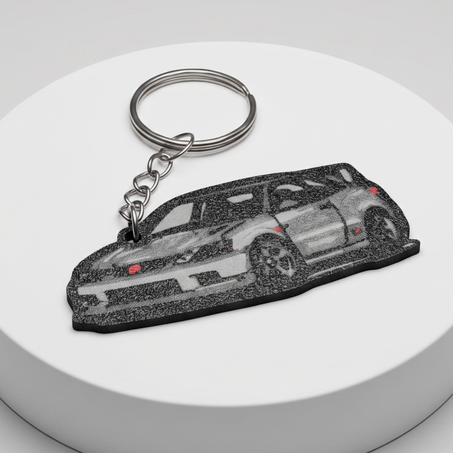 A car-shaped keychain with a silver split ring and chain, featuring a detailed grayscale illustration of a sports car, displayed on a round white pedestal against a light gray background.