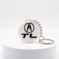 A white round keychain featuring the black Acura logo and 'TL' text, attached to a silver metal chain, displayed on a white cylindrical pedestal against a light gray background.