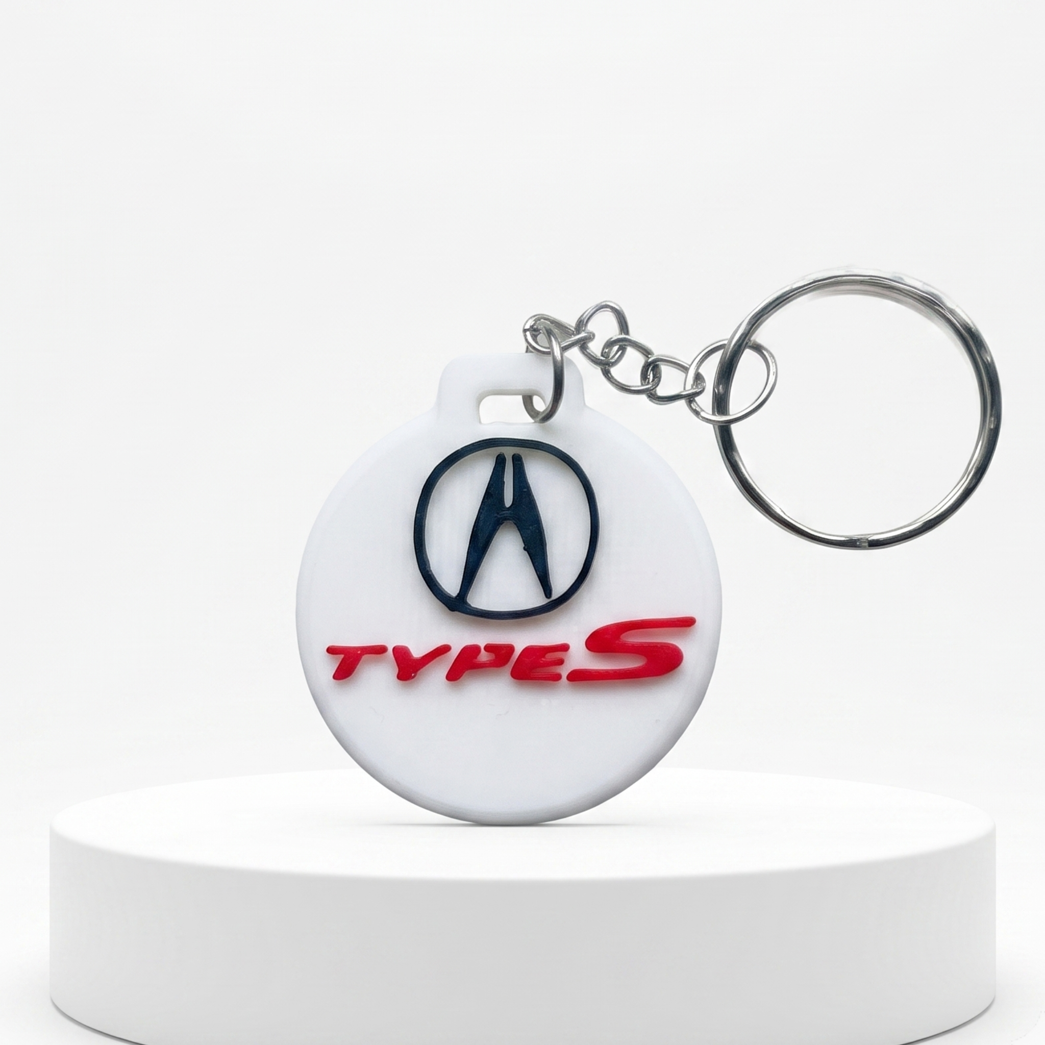 A white circular keychain featuring the Acura logo and 'TYPE S' text, attached to a silver split ring and displayed on a white pedestal.